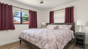 Quarto com cama, duas mesas de cabeceira, ventilador de teto e janela com cortinas.
