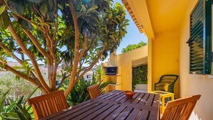 A wooden table and chairs set outdoors with a yellow wall and a green chair in the background. - Villa Caliços By Dreamplaces (Albufeira)