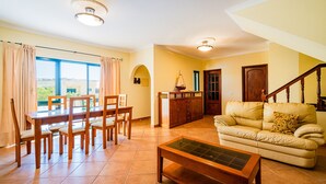 A spacious living area with a dining table, chairs, a sofa, and a staircase. - Villa Caliços By Dreamplaces (Albufeira)