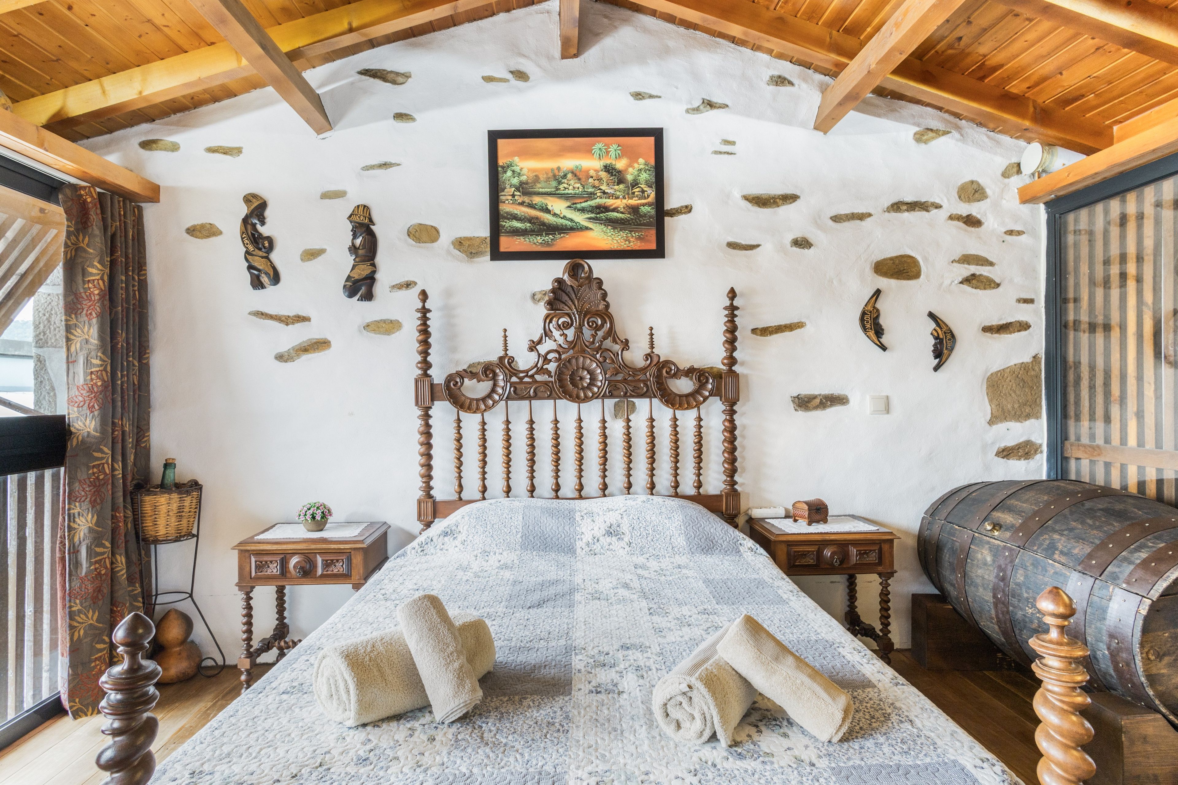 Une chambre à coucher rustique avec un mur en pierre, un cadre de lit en bois et un tableau représentant un paysage.