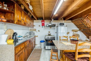 A compact kitchen with wooden cabinets, a built-in stove, a microwave, and a small dining area with a table and chairs. - Apartment 'Casa Alto Das Fragas' with Mountain View, Wi-Fi and Air Conditioning (Canedo de Basto)