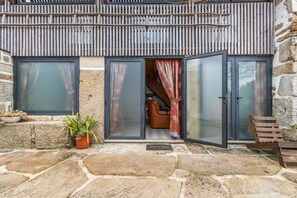A stone building with a wooden balcony, a sliding glass door entrance, and a welcome mat.