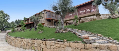 A stone-walled property with a sloped roof, a paved pathway, and a well-maintained lawn.