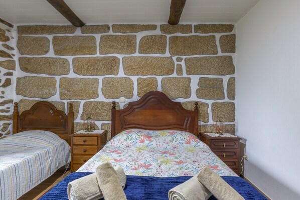 A bedroom with a stone wall, a wooden bed with a floral bedspread, and a nightstand with a lamp.