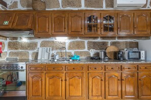 Une cuisine dotée de meubles en bois, d’un mur en pierre et de divers appareils électroménagers, notamment une cuisinière, un four à micro-ondes et une machine à café.