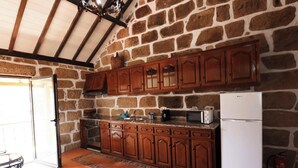 A kitchen with stone walls, wooden cabinets, a refrigerator, and a stove.