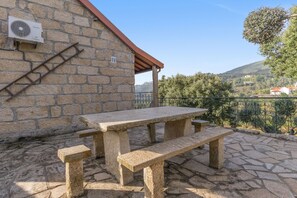 Une terrasse en pierre avec une table et des bancs, un mur en pierre et une vue sur la campagne.