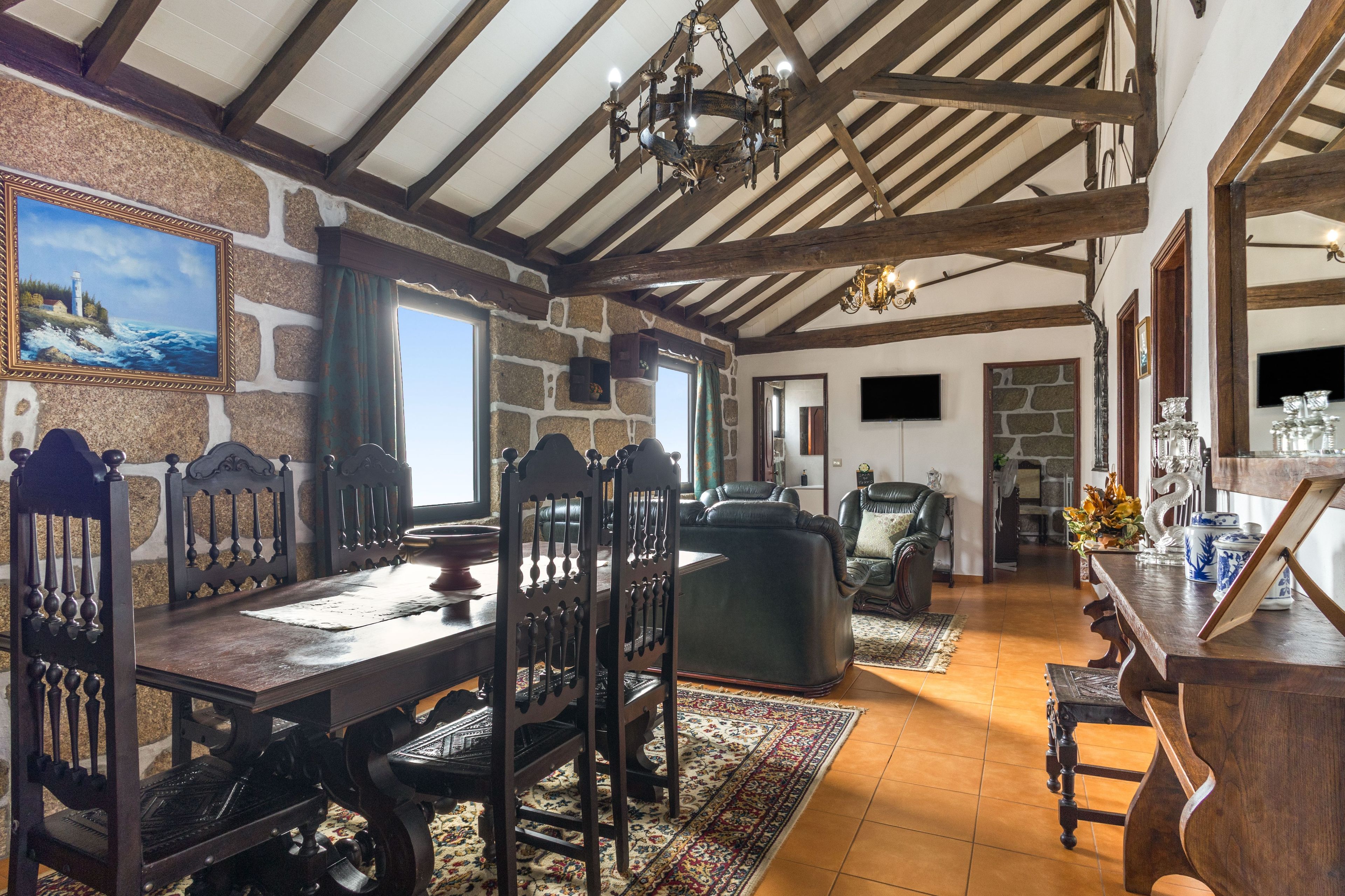 A dining area with a wooden table and chairs, a chandelier, and a stone wall.