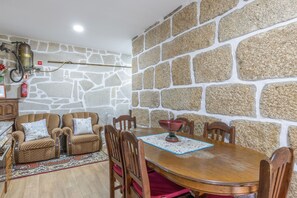 A dining area with a stone wall, wooden chairs, a table, and a fire extinguisher.