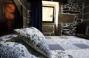 A room with a stone wall, a window with a view, and a bed with floral bedding. - Casa Do Vale JC - Sobreiro (Vila Nune)