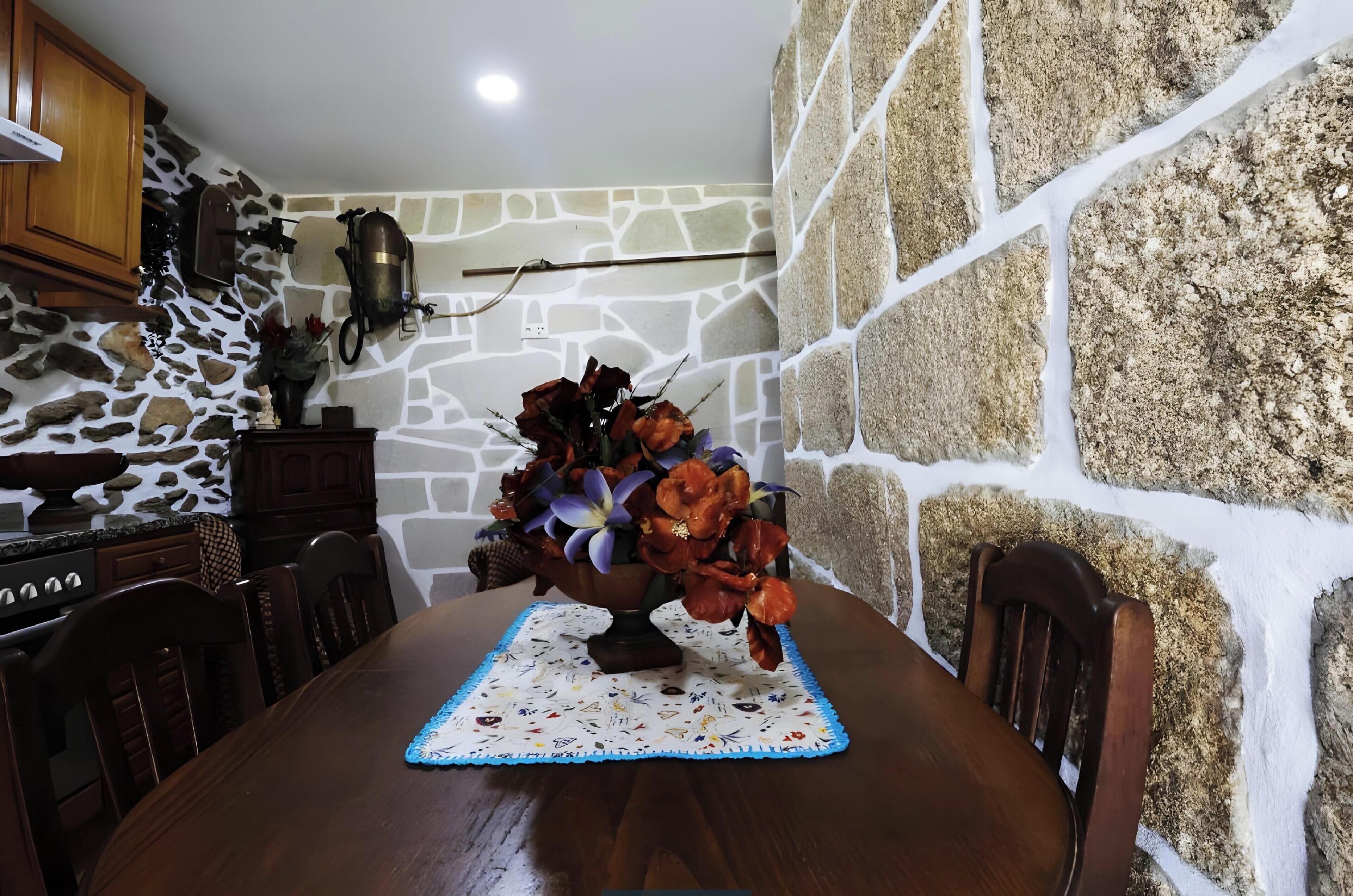 A dining table with a floral centerpiece, stone walls, and wooden furniture.