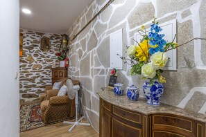 A room with a stone wall, a wooden cabinet, a wicker sofa, and a small table with decorative items. - Casa Do Vale JC - Sobreiro (Vila Nune)