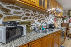 A kitchen with granite countertops, wooden cabinets, a stone wall, and a stainless steel sink. - Casa Do Vale JC - Sobreiro (Vila Nune)