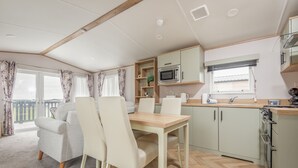 A compact kitchen with a dining area, wooden cabinets, a microwave, and a window with blinds.