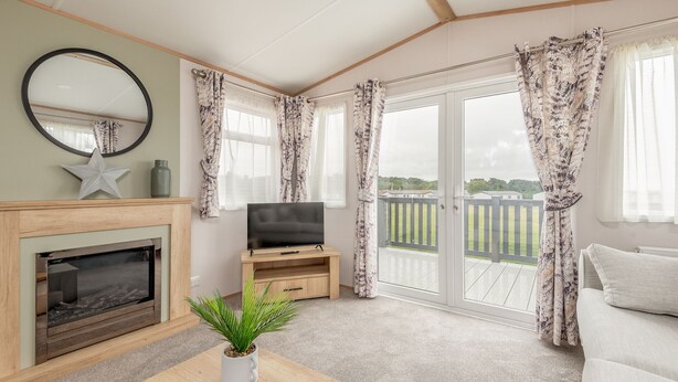 A living room with a fireplace, a television, and a balcony with a view of greenery.