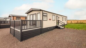 A mobile home with a fenced deck, a small staircase, and a gravel driveway.