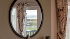 A round mirror with a view of a beach through a window with curtains.