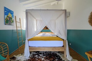 Ein Zimmer mit einem Bett unter einem weißen Baldachin, einer Holzleiter, einem Kuhfellteppich und einem Bild an der Wand.