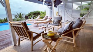 A covered outdoor seating area with wooden furniture, a pool, and a view of the ocean.