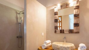 A bathroom with a shower, a sink with a stone basin, and a mirror with a wooden frame.