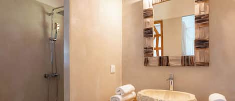 Une salle de bain avec une douche, un lavabo doté d’un receveur en pierre et un miroir avec un cadre en bois.