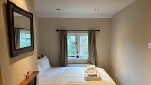 Une chambre à coucher avec un lit, une table de chevet, un miroir et une fenêtre avec des rideaux.
