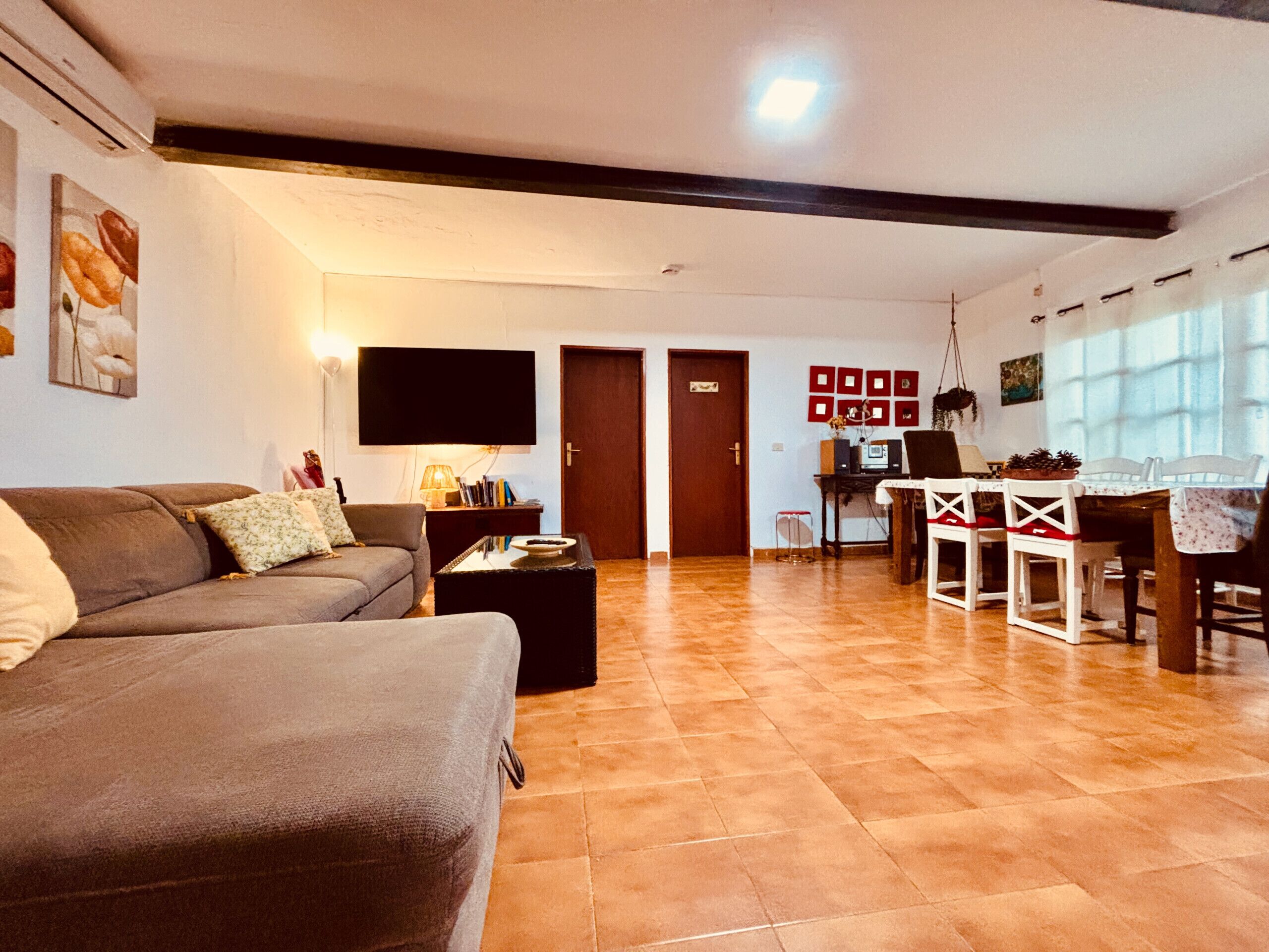 A living room with a sofa, a coffee table, and a TV. There is a dining area with a table and chairs.