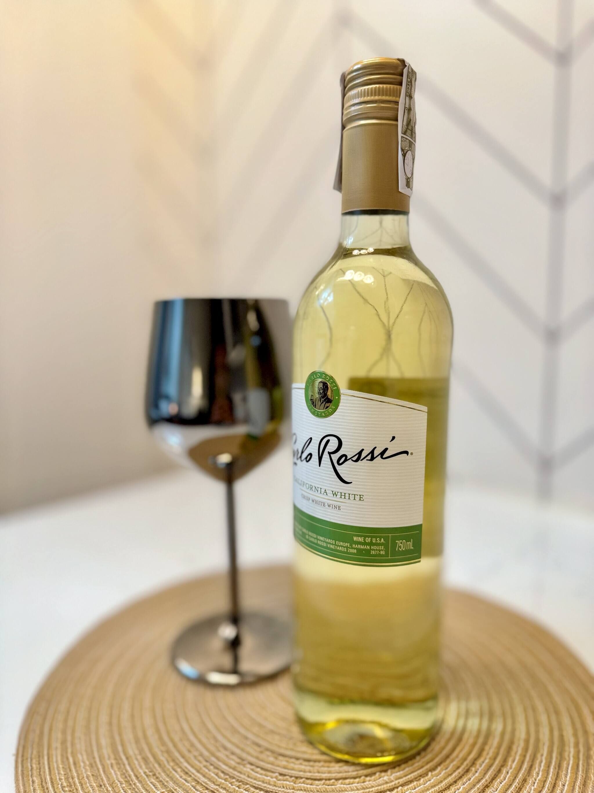 Una bottiglia di vino bianco Carlo Rossi California, con un bicchiere da vino accanto, su un sottopiattino intrecciato.