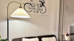 Un salon moderne avec un canapé, des coussins décoratifs, une lampe sur pied et deux œuvres d’art murales.