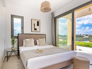 Ein modernes Schlafzimmer mit einem großen Bett, einem Glastisch, einer Zimmerpflanze und Blick auf die Stadt.