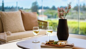 A table with two glasses of white wine, a vase with pink flowers, and a wooden board with cheese and crackers. - Sanders Limassol Park - Full Building (Trachoni)