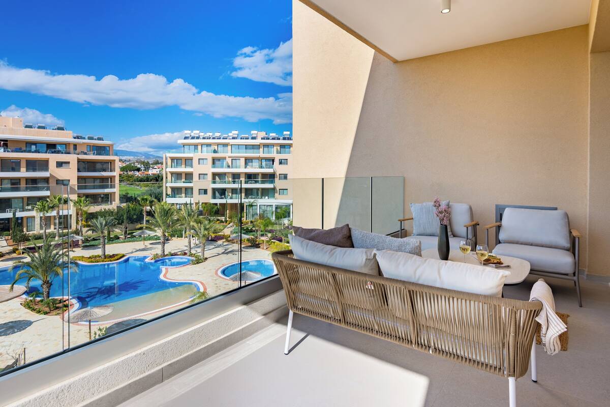 A modern hotel room with a balcony overlooking a swimming pool and other buildings.