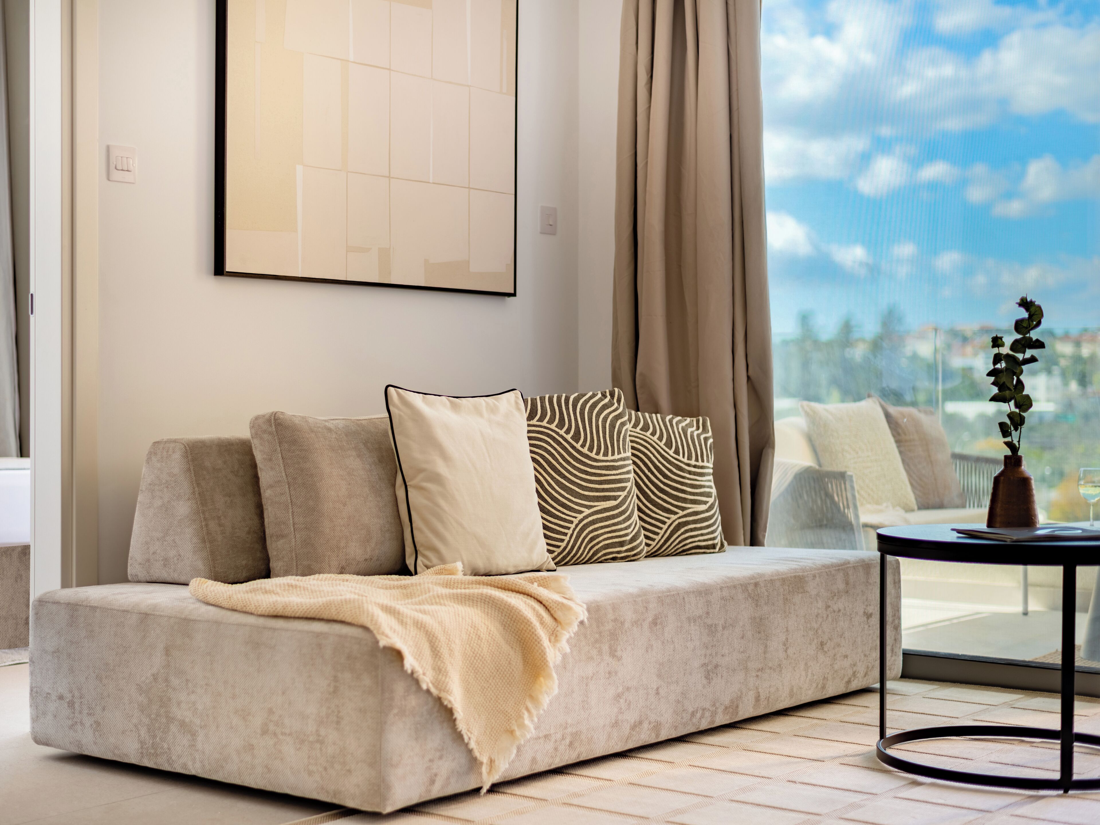 A modern living room with a sofa, a coffee table, and a view of the sky.