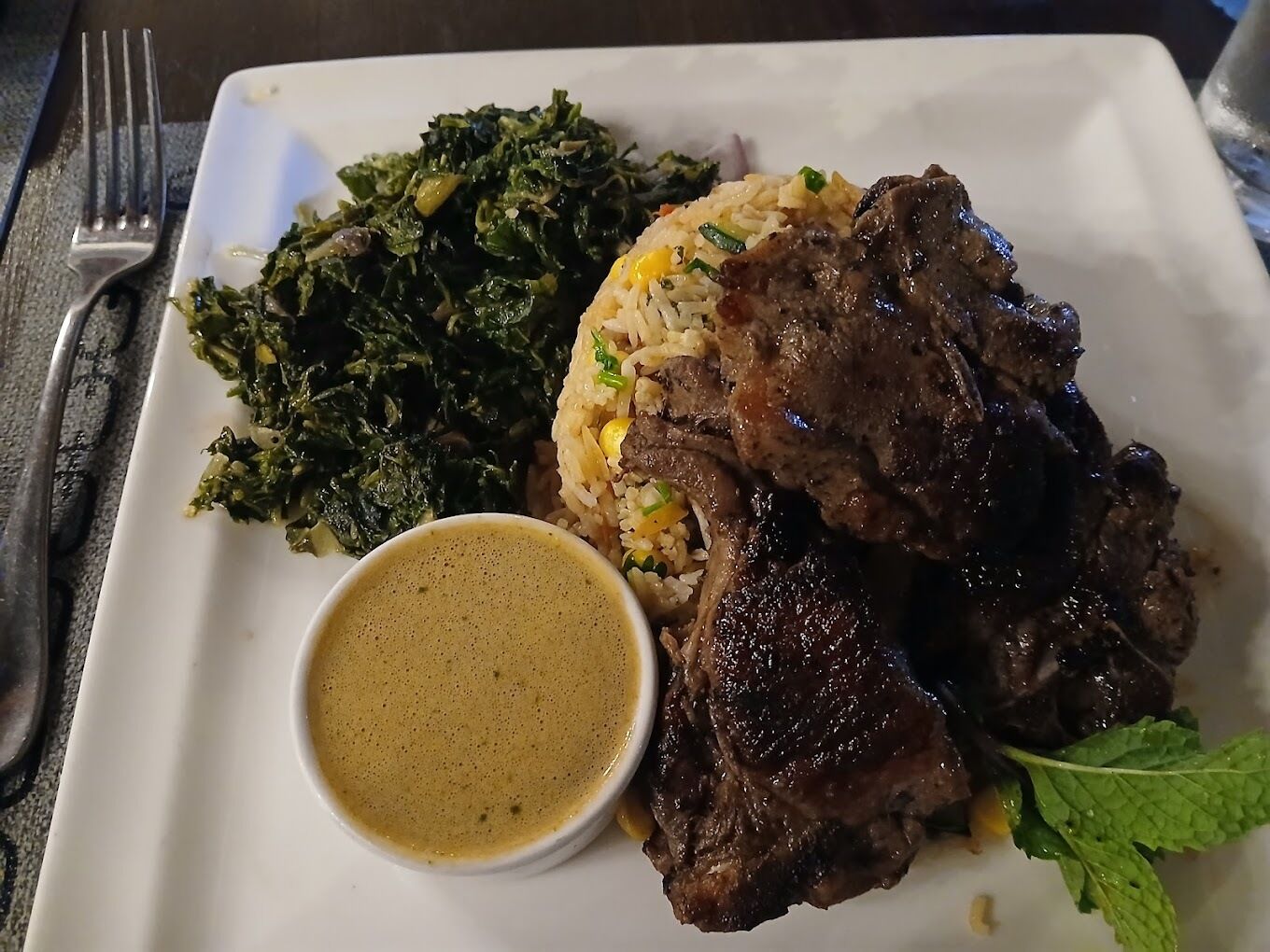 Une assiette contenant un plat de bœuf, des légumes verts et du riz, accompagnée d’un petit bol de sauce.