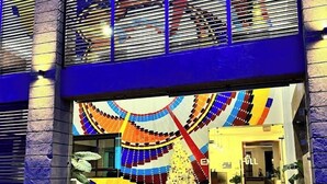 A modern building with a colorful, abstract mural on the facade, a set of stairs leading to the entrance, and a small outdoor fountain. - Enkipai Hill Hotel (Narok)