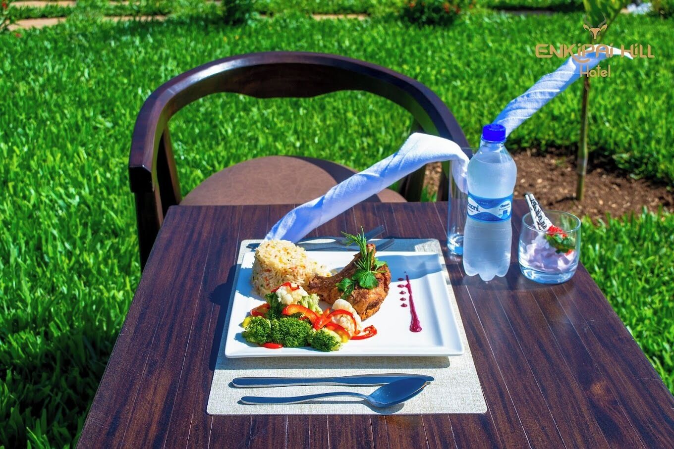A meal on a wooden table with a chair, a bottle of water, and a glass with a straw.
