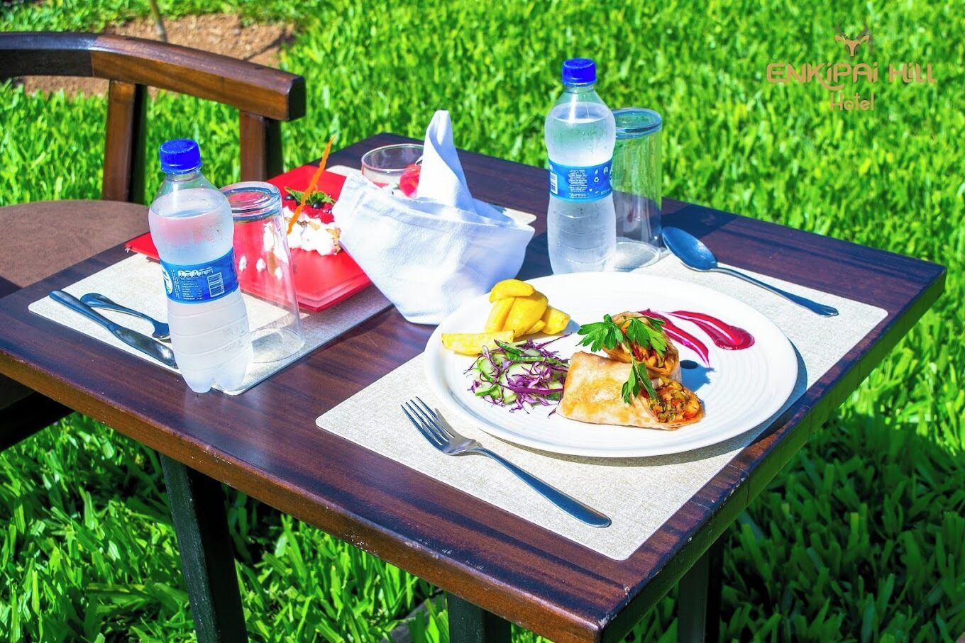 Una mesa al aire libre con comida, botellas de agua y un vaso.