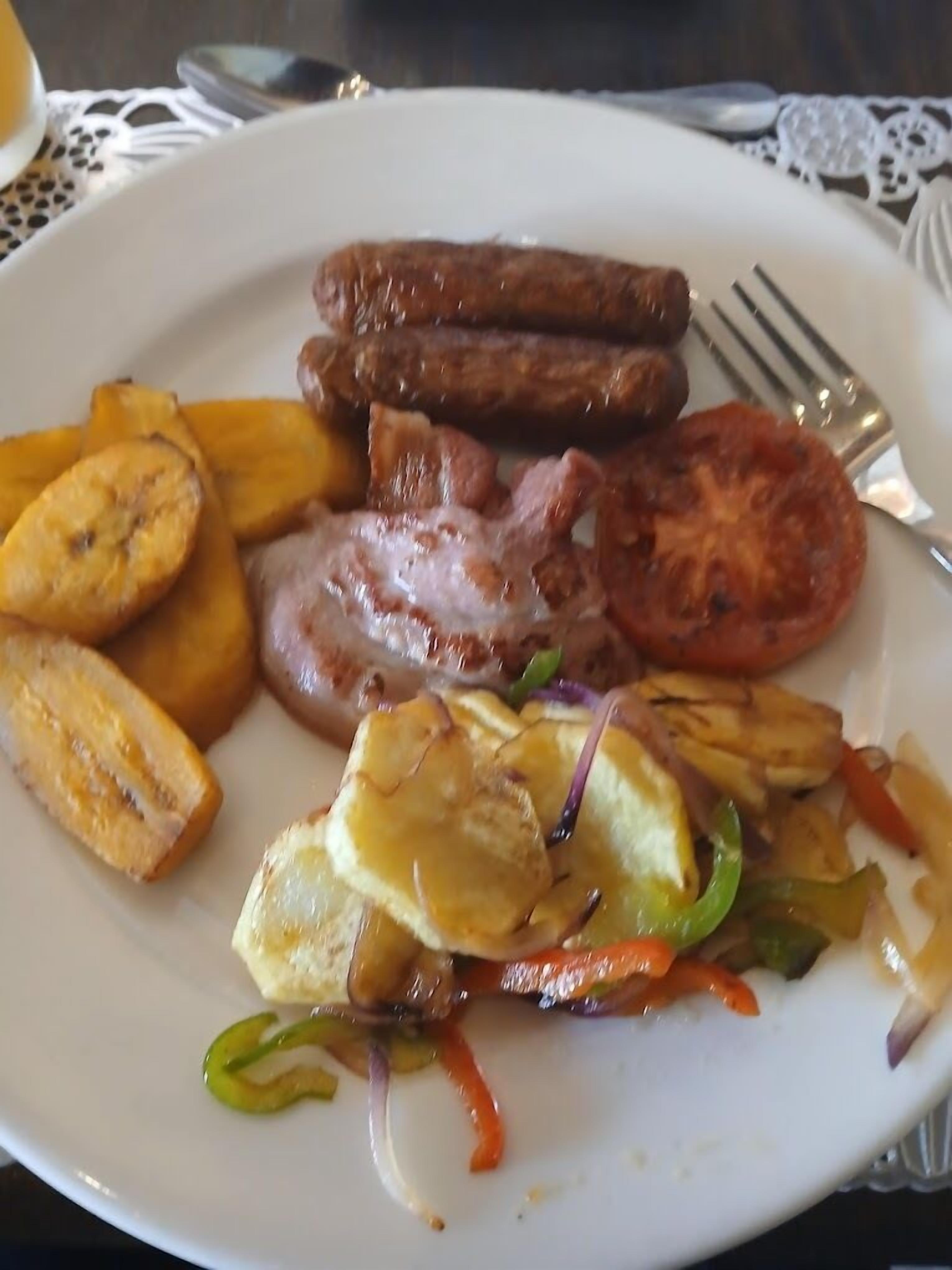 Un plato de comida con salchichas, tocino, tomates y plátanos fritos.
