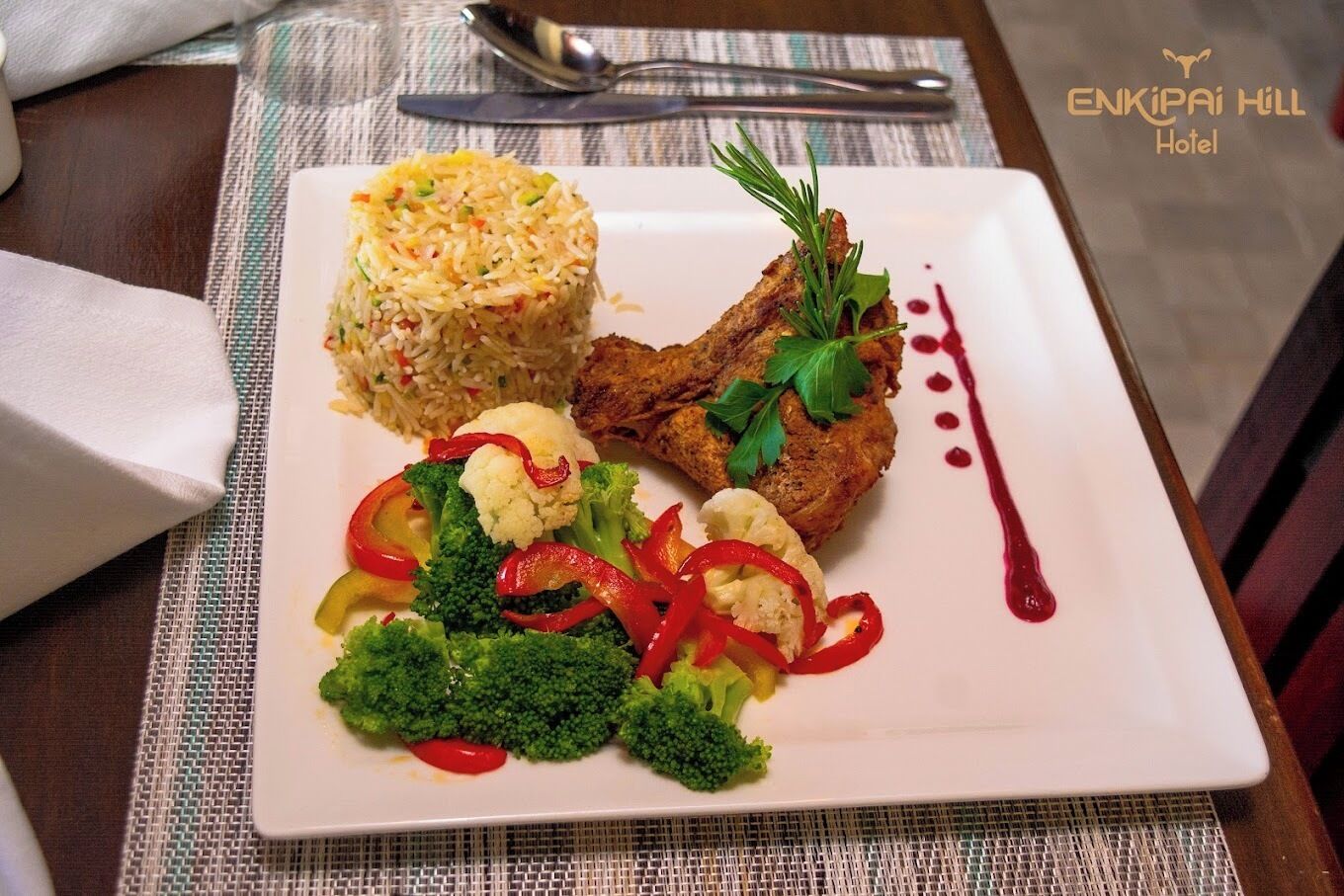 A plate of food with rice, meat, and vegetables on a table with a placemat and a spoon.