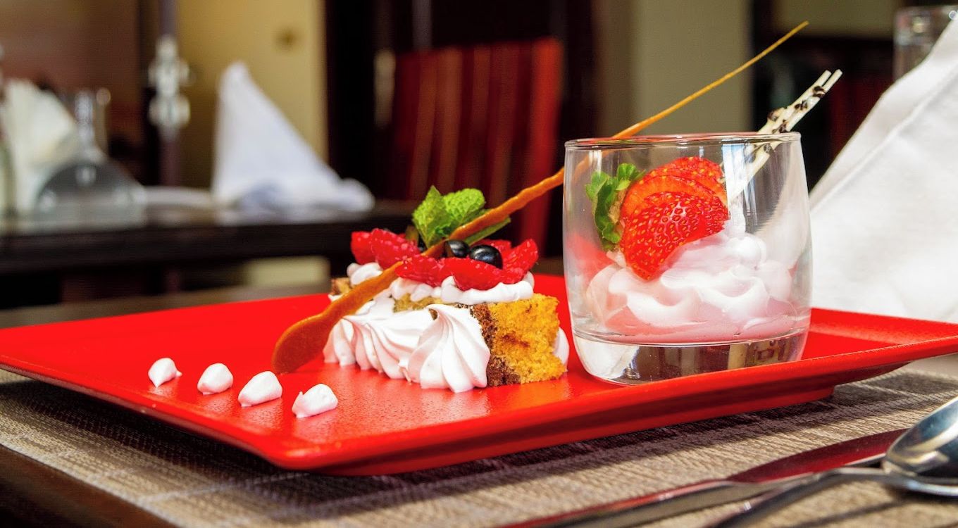 A dessert on a red tray with a glass of dessert drink, ENKIPAI HILL HOTEL logo, and a spoon on a table.