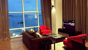 A living room with a large window, a sofa, two red chairs, a coffee table, and a flat-screen TV. - Urbano Luxury Homestay (George Town)