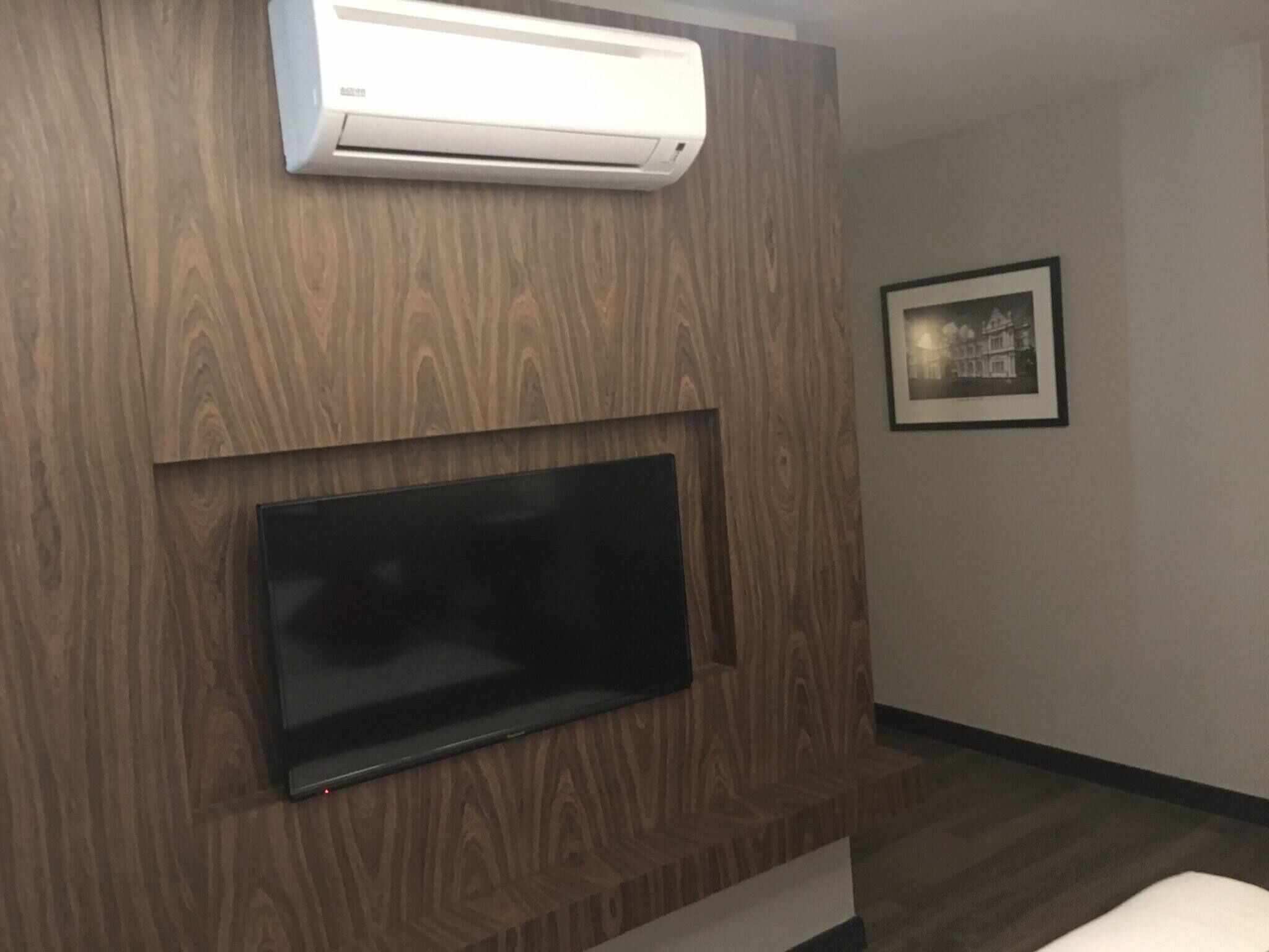 A modern living room with a mounted flat-screen TV, a built-in air conditioning unit, and a framed picture on the wall.