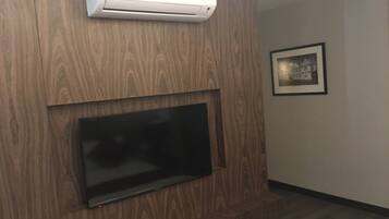 A modern living room with a mounted flat-screen TV, a built-in air conditioning unit, and a framed picture on the wall.