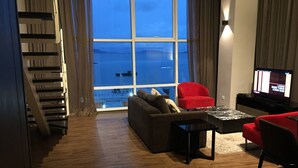 A modern living room with a large window, a sofa, a red chair, and a television. - Urbano Luxury Homestay (George Town)