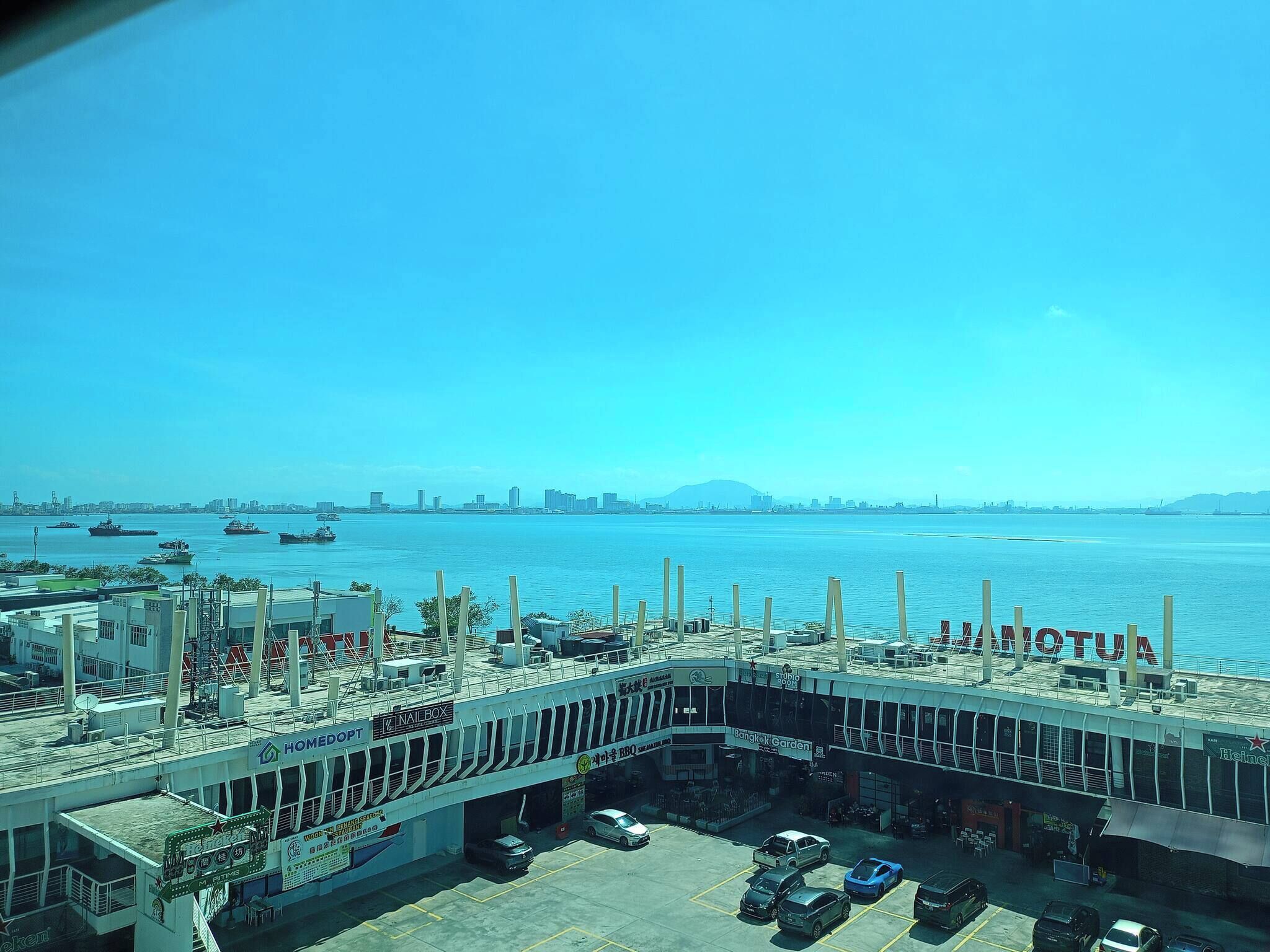 A waterfront view with a parking area, a building with a sign reading "Bangkok Garden," and several boats on the water.