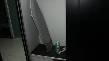 A room with a white ironing board, a green iron, and a white drawer unit.