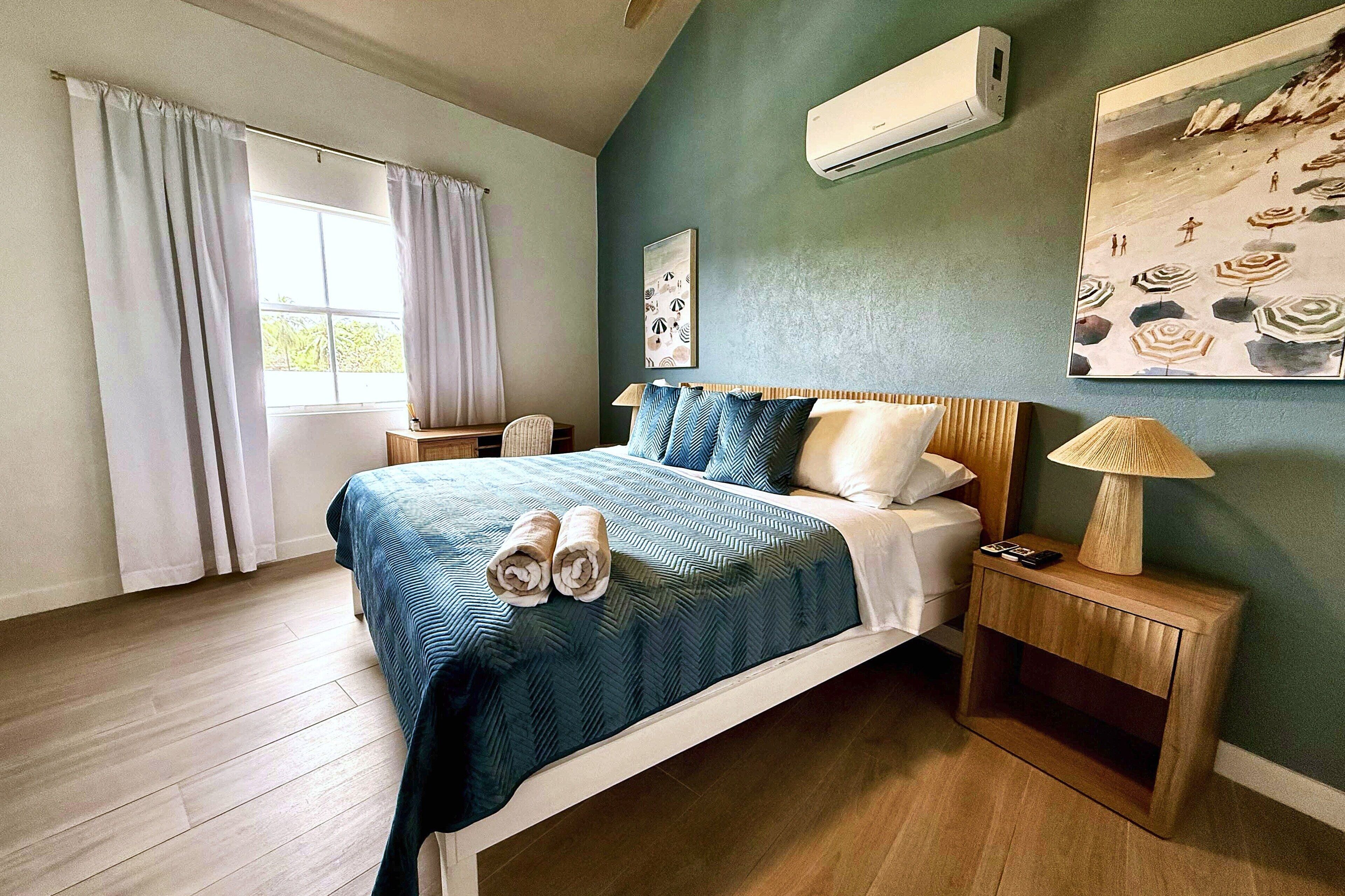 Un dormitorio con cama, mesitas de noche, lámpara y cuadros en la pared.