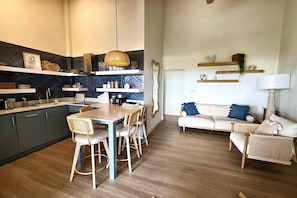 A modern kitchen with a dining area, featuring a wooden table, chairs, and a hanging light fixture. - Lantana Sea La Vie - by Zenbreak (Weston)