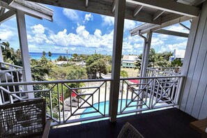 Un espacio al aire libre techado con piscina, terraza de madera y vista al océano y palmeras.