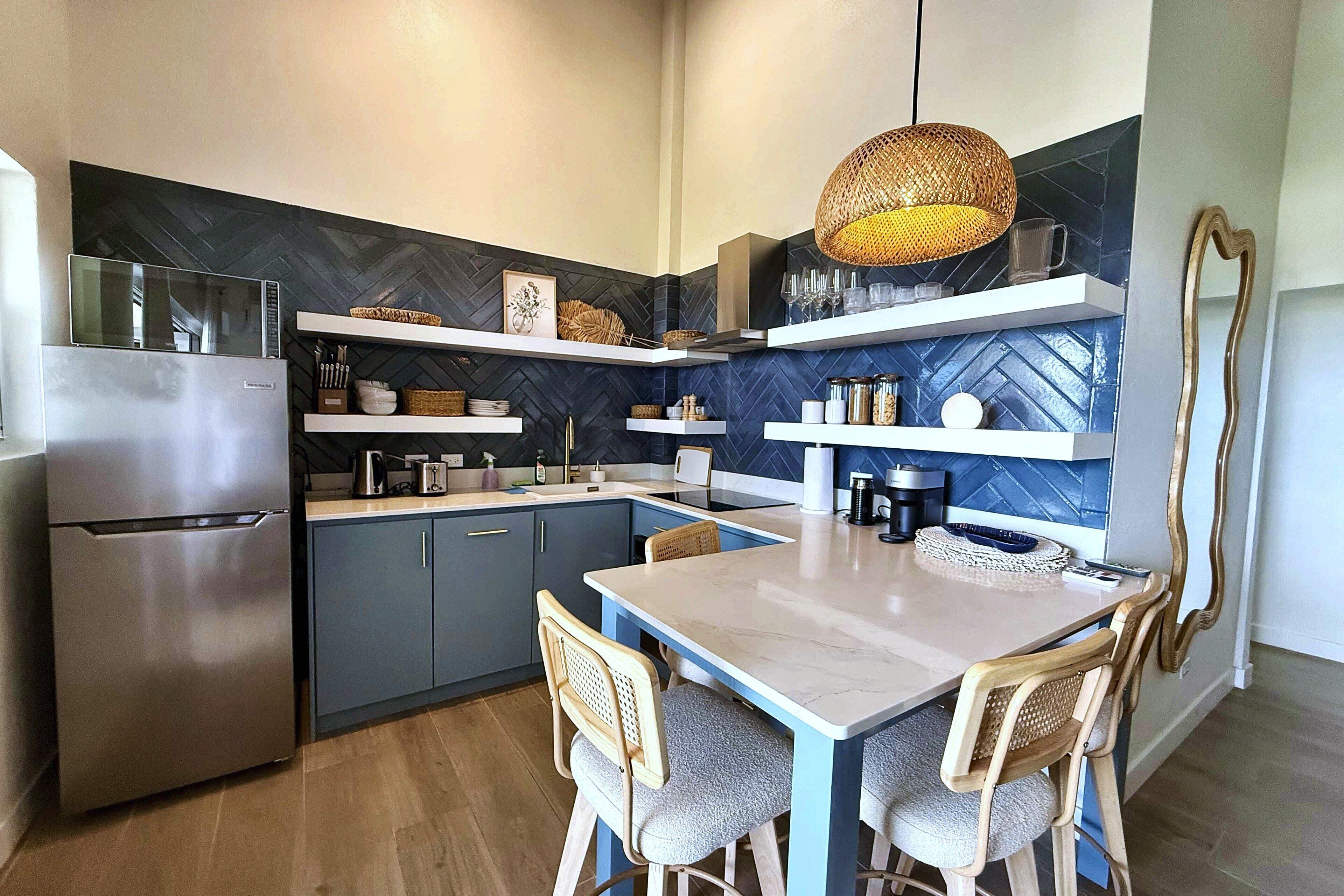 A modern kitchen with a built-in refrigerator, wooden chairs, a dining table, and decorative shelves.